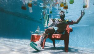 man sitting on chair underwater with floating bottles